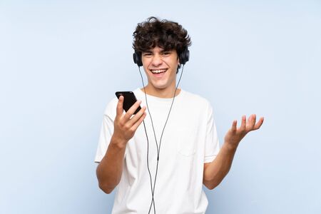 Young man listening music with a mobile over isolated blue wallの写真素材
