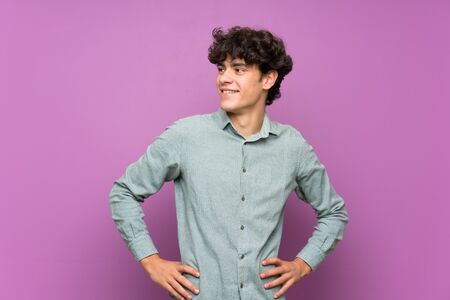Young man over isolated purple wall posing with arms at hip and smilingの写真素材
