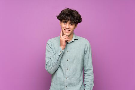 Young man over isolated purple wall thinking an idea while looking upの写真素材