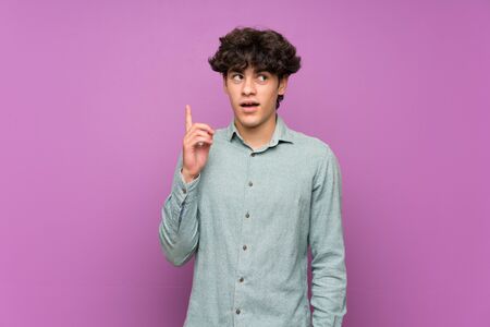 Young man over isolated purple wall thinking an idea pointing the finger upの写真素材