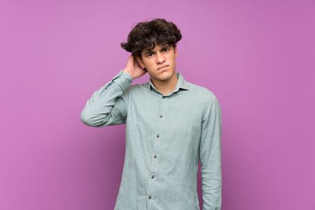 Young man over isolated purple wall having doubtsの写真素材
