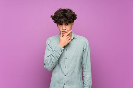 Young man over isolated purple wall thinkingの写真素材