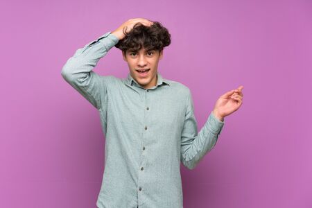 Young man over isolated purple wall surprised and pointing finger to the sideの写真素材