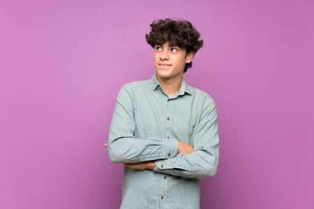 Young man over isolated purple wall looking up while smilingの写真素材