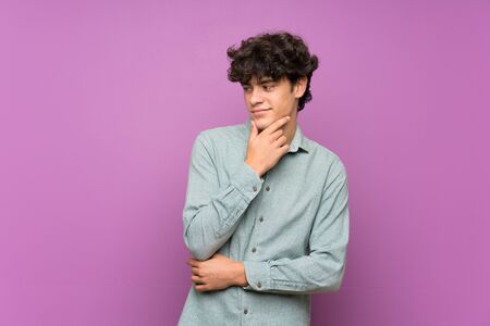 Young man over isolated purple wall looking to the sideの写真素材