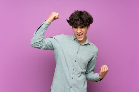 Young man over isolated purple wall celebrating a victoryの写真素材