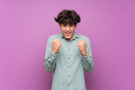 Young man over isolated purple wall celebrating a victory in winner positionの写真素材