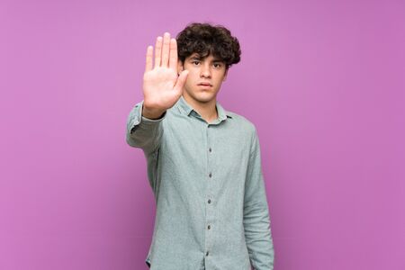 Young man over isolated purple wall making stop gestureの写真素材