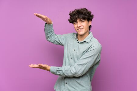 Young man over isolated purple wall holding copyspace to insert an adの写真素材
