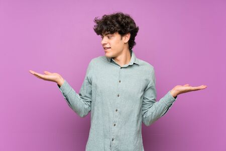 Young man over isolated purple wall holding copyspace with two handsの写真素材