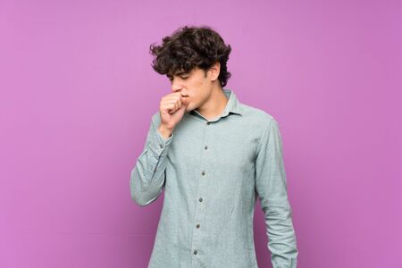 Young man over isolated purple wall is suffering with cough and feeling badの写真素材