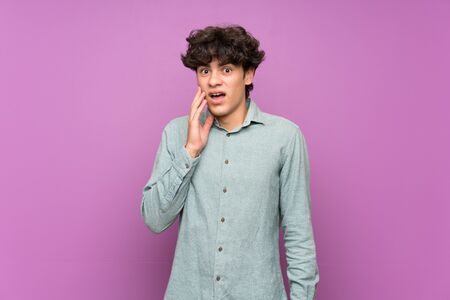 Young man over isolated purple wall with surprise and shocked facial expressionの写真素材