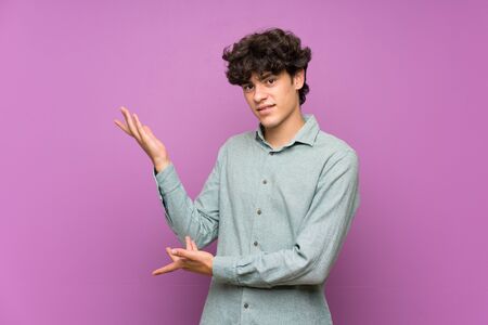 Young man over isolated purple wall extending hands to the side for inviting to comeの写真素材