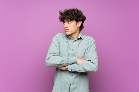 Young man over isolated purple wall making doubts gesture while lifting the shouldersの写真素材