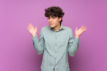 Young man over isolated purple wall making doubts gestureの写真素材