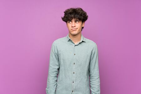 Young man over isolated purple wall making doubts gesture looking sideの写真素材