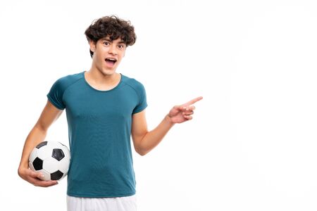 Young football player man over isolated white wall surprised and pointing finger to the sideの写真素材