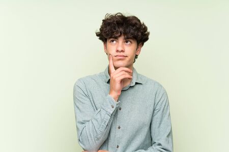 Young man over isolated green wall thinking an ideaの写真素材