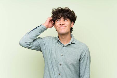 Young man over isolated green wall having doubts and with confuse face expressionの写真素材