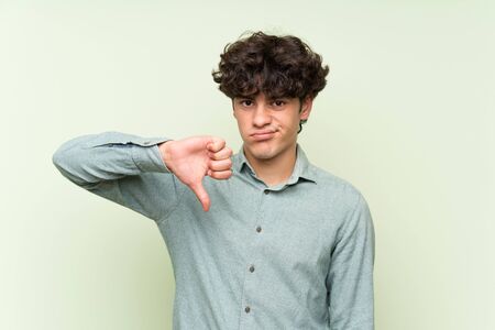 Young man over isolated green wall showing thumb down signの写真素材