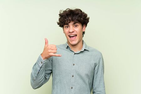 Young man over isolated green wall making phone gestureの写真素材