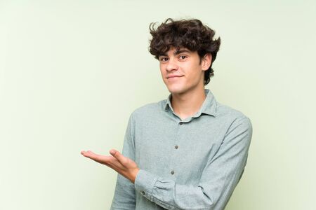 Young man over isolated green wall extending hands to the side for inviting to comeの写真素材