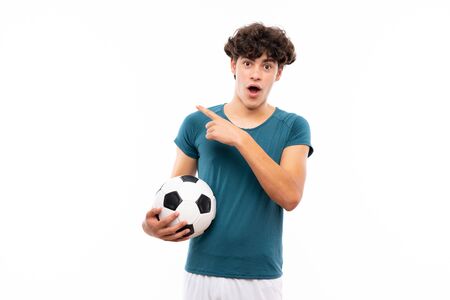 Young football player man over isolated white wall surprised and pointing sideの写真素材
