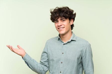 Young man over isolated green wall holding copyspace imaginary on the palmの写真素材