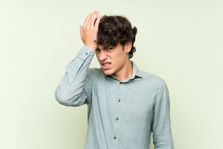Young man over isolated green wall having doubts with confuse face expressionの写真素材