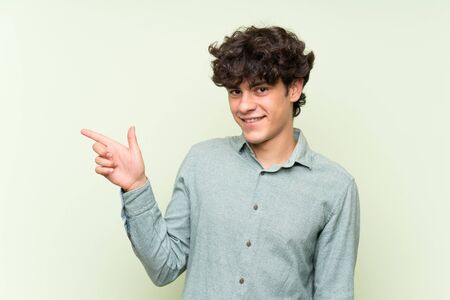 Young man over isolated green wall pointing finger to the sideの写真素材