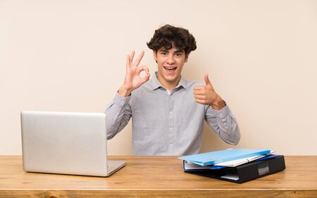 Young student man with a laptop showing ok sign and thumb up gestureの写真素材