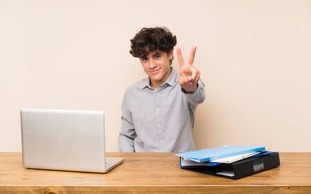 Young student man with a laptop smiling and showing victory signの写真素材