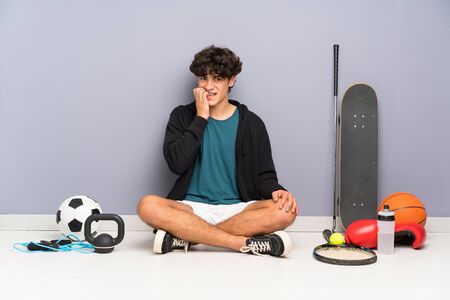 Young sport man sitting on the floor around many sport elements nervous and scaredの写真素材