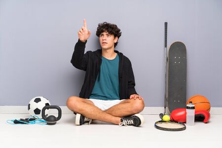 Young sport man sitting on the floor around many sport elements touching on transparent screenの写真素材