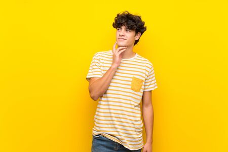 Young man over isolated yellow wall thinking an idea while looking upの写真素材