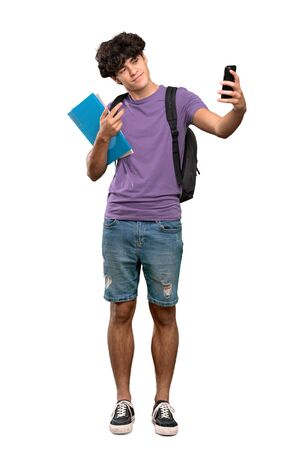 A full-length shot of a Young student man making a selfie over isolated white backgroundの写真素材