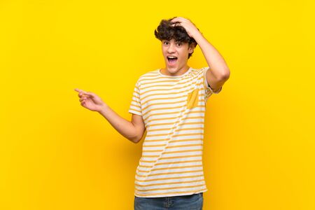 Young man over isolated yellow wall surprised and pointing finger to the sideの写真素材