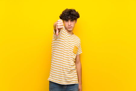 Young man over isolated yellow wall showing thumb down with negative expressionの写真素材