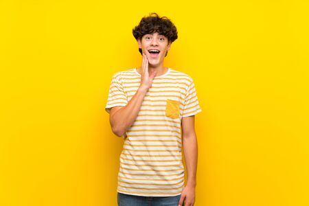 Young man over isolated yellow wall with surprise and shocked facial expressionの写真素材