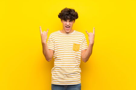 Young man over isolated yellow wall making rock gestureの写真素材