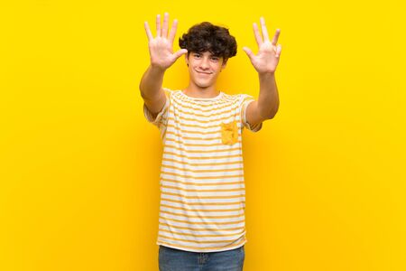 Young man over isolated yellow wall counting nine with fingersの写真素材