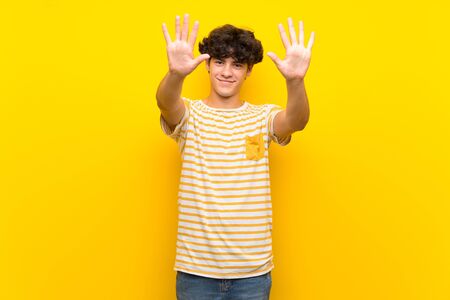 Young man over isolated yellow wall counting ten with fingersの写真素材