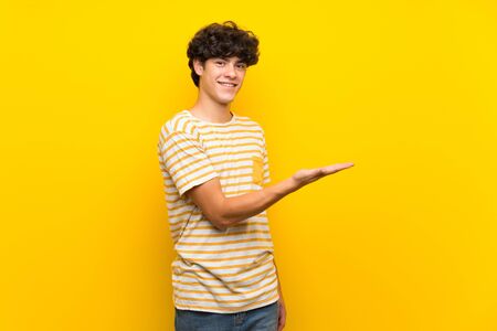 Young man over isolated yellow wall presenting an idea while looking smiling towardsの写真素材