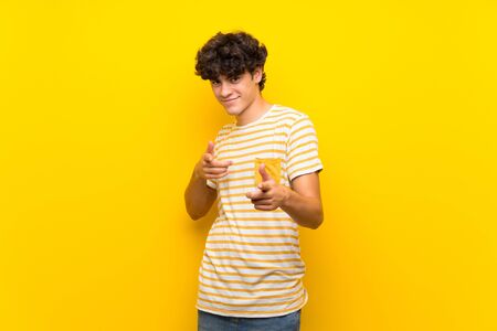 Young man over isolated yellow wall pointing to the front and smilingの写真素材