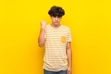 Young man over isolated yellow wall with angry gestureの写真素材