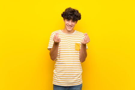 Young man over isolated yellow wall making money gestureの写真素材