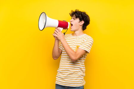 Young man over isolated yellow wall shouting through a megaphoneの写真素材