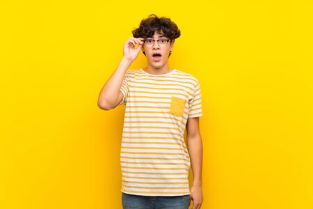 Young man over isolated yellow wall with glasses and surprisedの写真素材