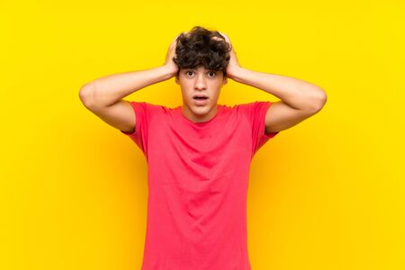 Young man over isolated yellow wall with surprise facial expressionの写真素材