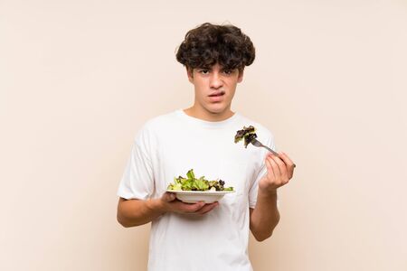 Young man with salad over isolated green wallの写真素材